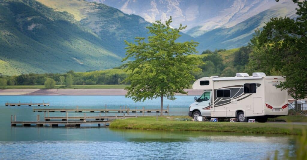 RV is parked at the bank of lake in the mountains showcasing its 25 feet length.