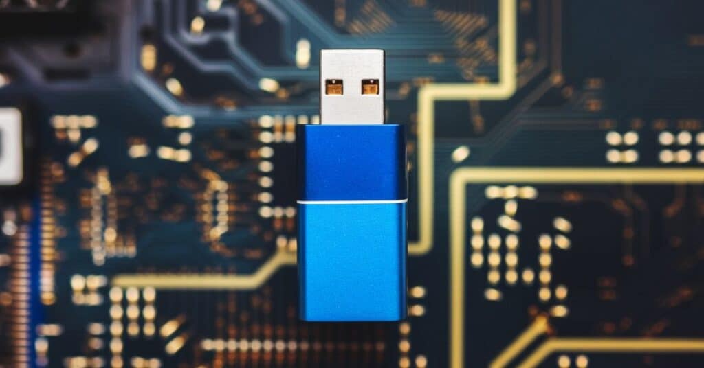 A photo of a USB flash drive against a background of 
 blurred computer circuitry. The USB flash drive has a blue body with a silver top.