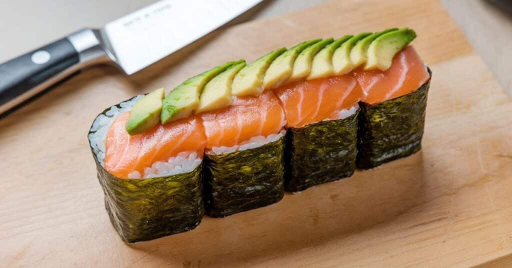 A sushi roll on the wooden cuting board showcasing its length of 15 centimeters before cutting