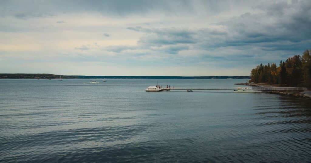 A photo of Lake Michigan on a cloudy day. The water is calm, with a few boats on the lake. A pier extends into the water, with a few people standing on it.