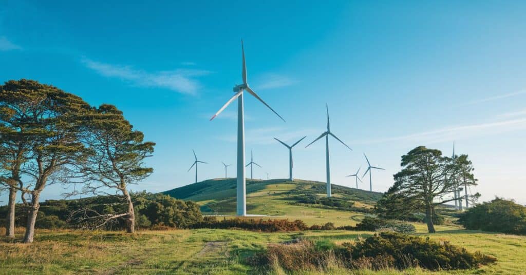 A landscape shot of 500 feet long wind turbines on a hilltop, with a clear blue sky in the background.