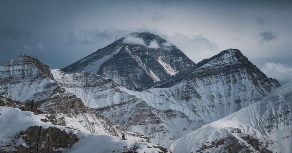 A photo of Mount Everest on a snowy day, with the peak partially covered by clouds. The mountain is covered in snow.