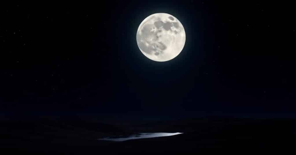 A stunning picture of the moon's radiant glow, illuminating the landscape below. The foreground features a peaceful lake reflecting the moonlight, enhancing the overall beauty.