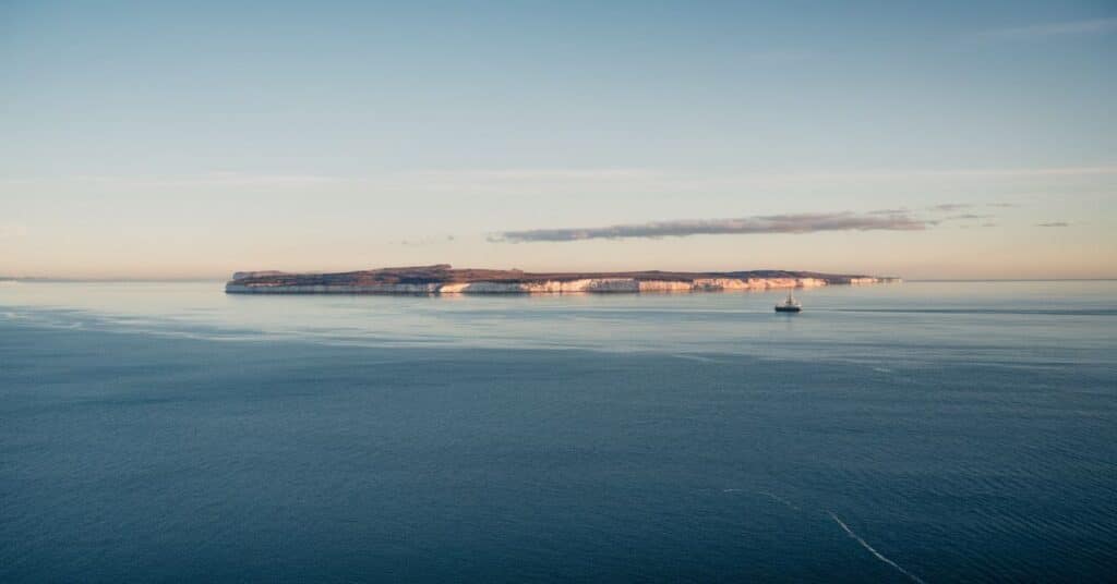 A photo of the Eastern North Sea with a calm sea and a clear sky. In the distance, there are islands with white cliffs. There is a ship in the sea.