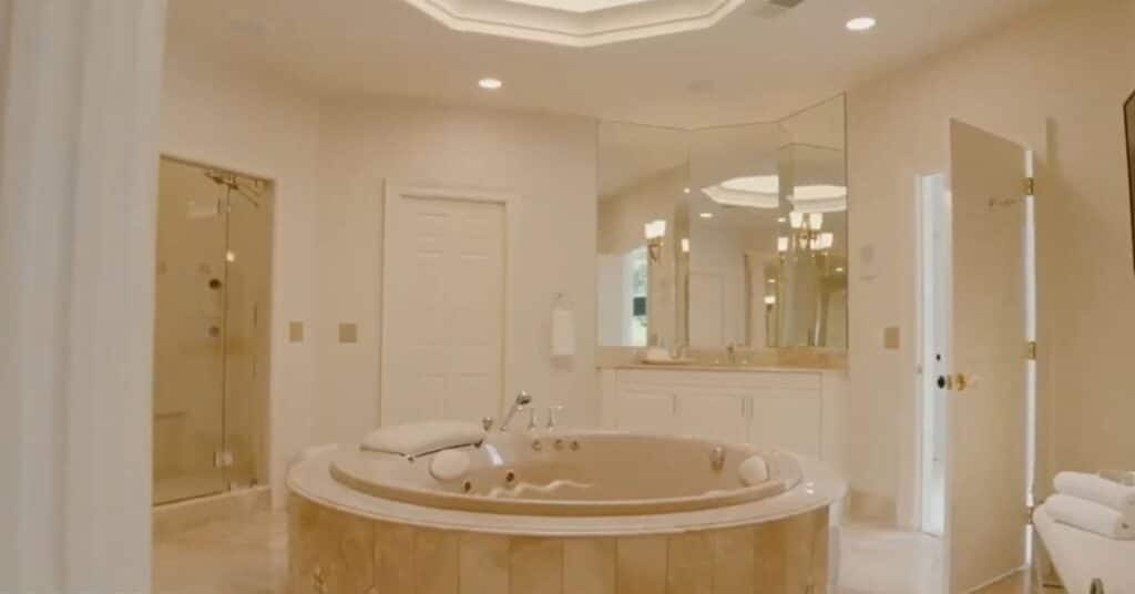 A picture of the bathroom of Mike's mansion. It is a off white and beige themed bathroom with good lightning and bathtub.