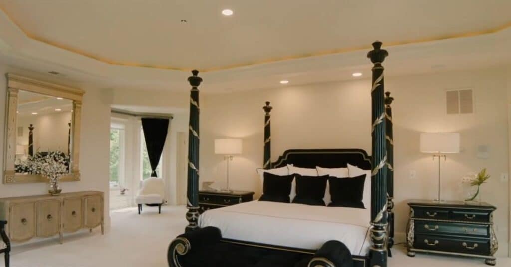 A picture of the master suite of Mike's home. The bed is black and covered with white bedsheet.