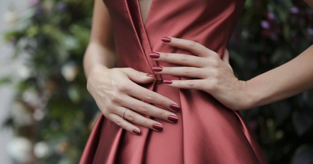 A photo of a lady with nails that match the color of her dress. The dress is a deep red hue, and her nails are also painted with the same shade.