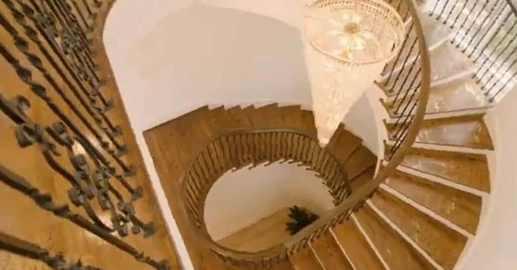 In picture, spiral staircase is shown in mike tyson house. The stairs are made up of wood and a chandelier is hung in between the stairs.