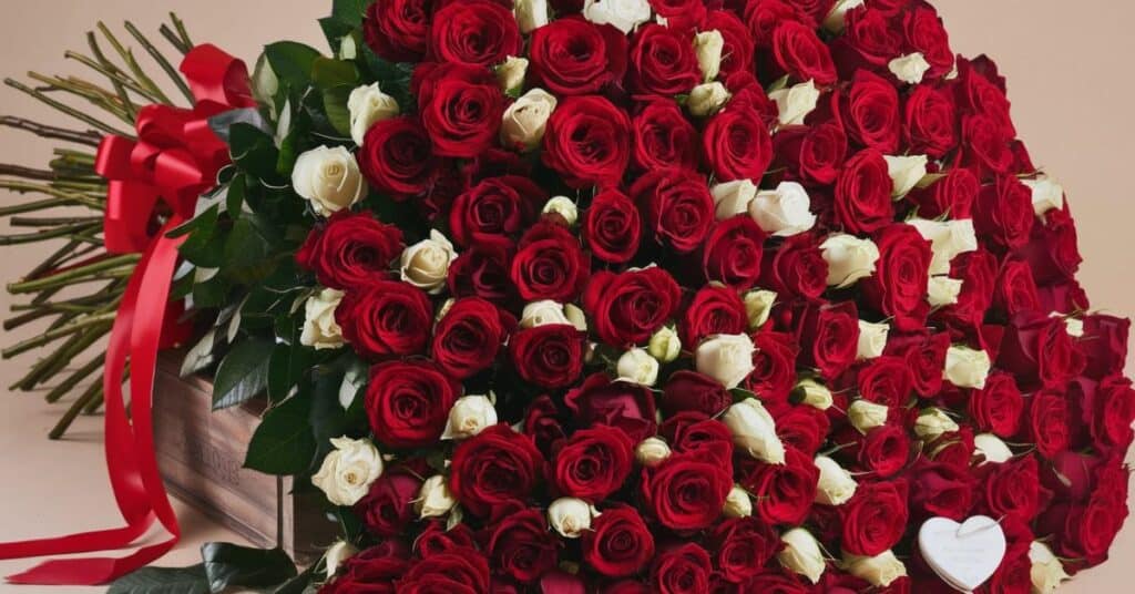 A massive bouquet of red roses with a few white roses mixed in. The bouquet is tied with a red ribbon and has a few leaves at the bottom.