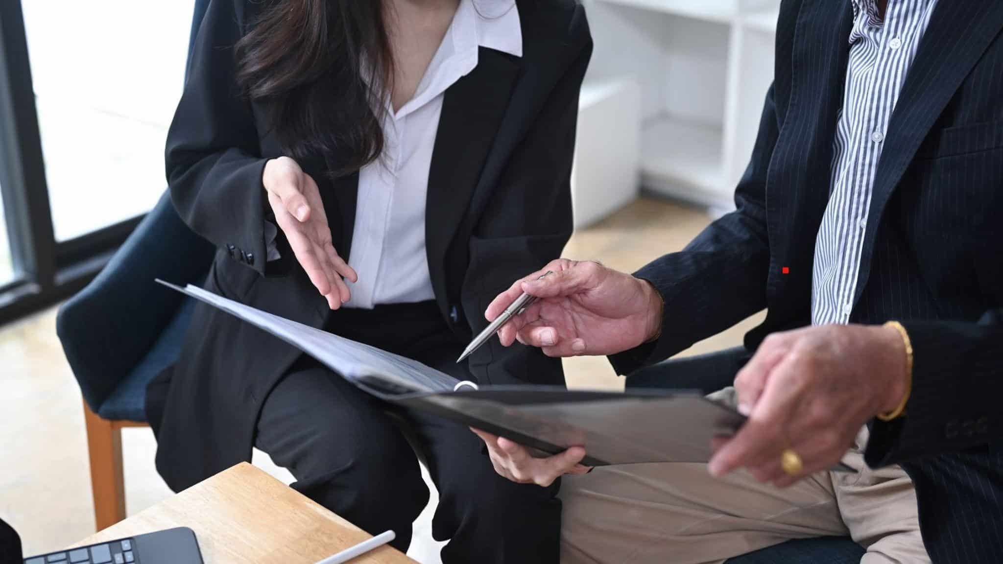 Dos profesionales con vestimenta formal revisando y discutiendo documentos juntos
